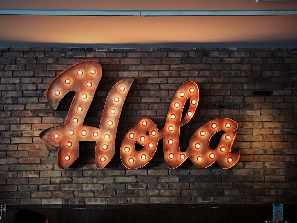 Sign on Brick Wall Saying Hello (Hola) in Spanish